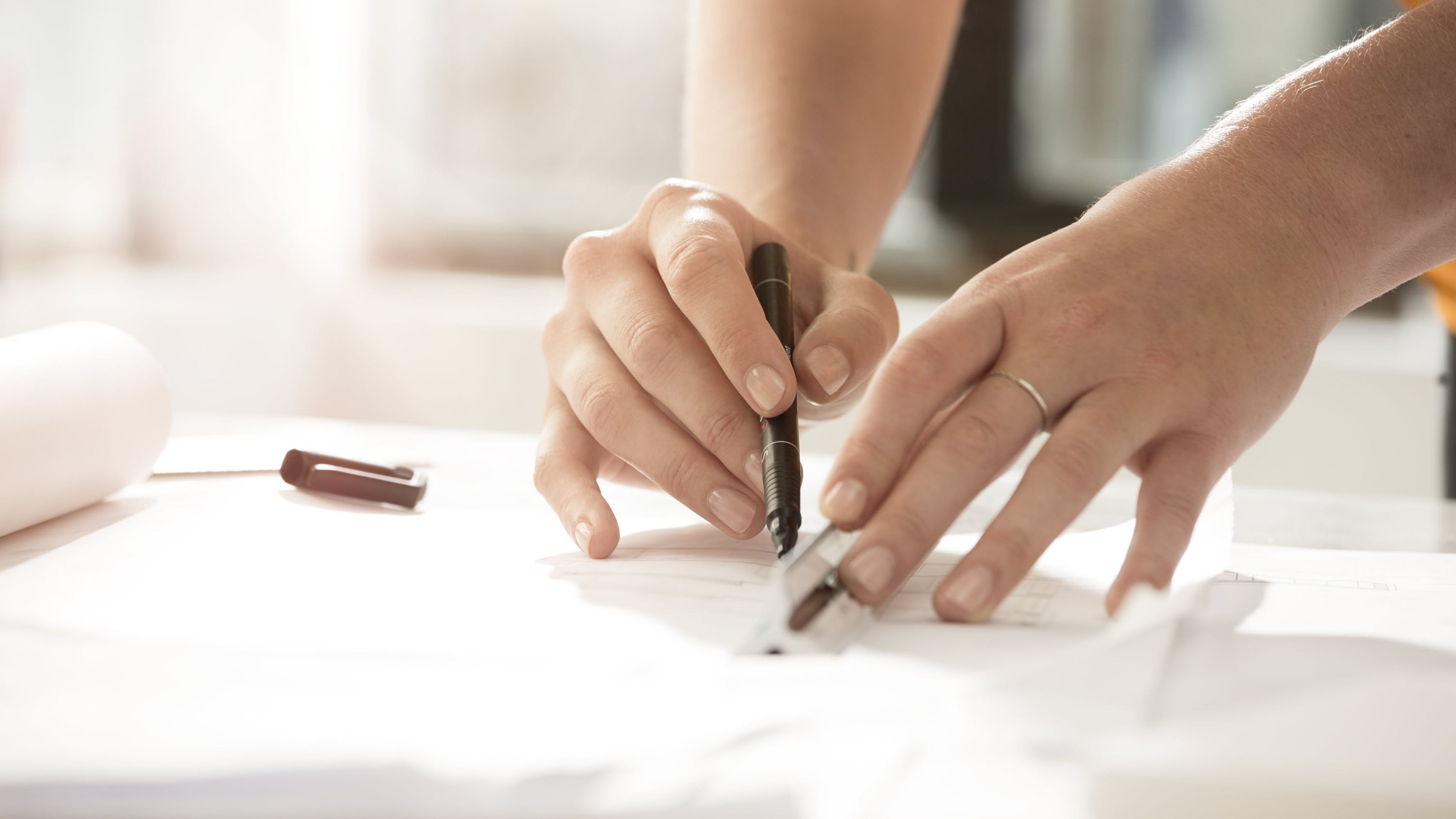 two hands drawing a line on a piece of paper with a pen and ruler