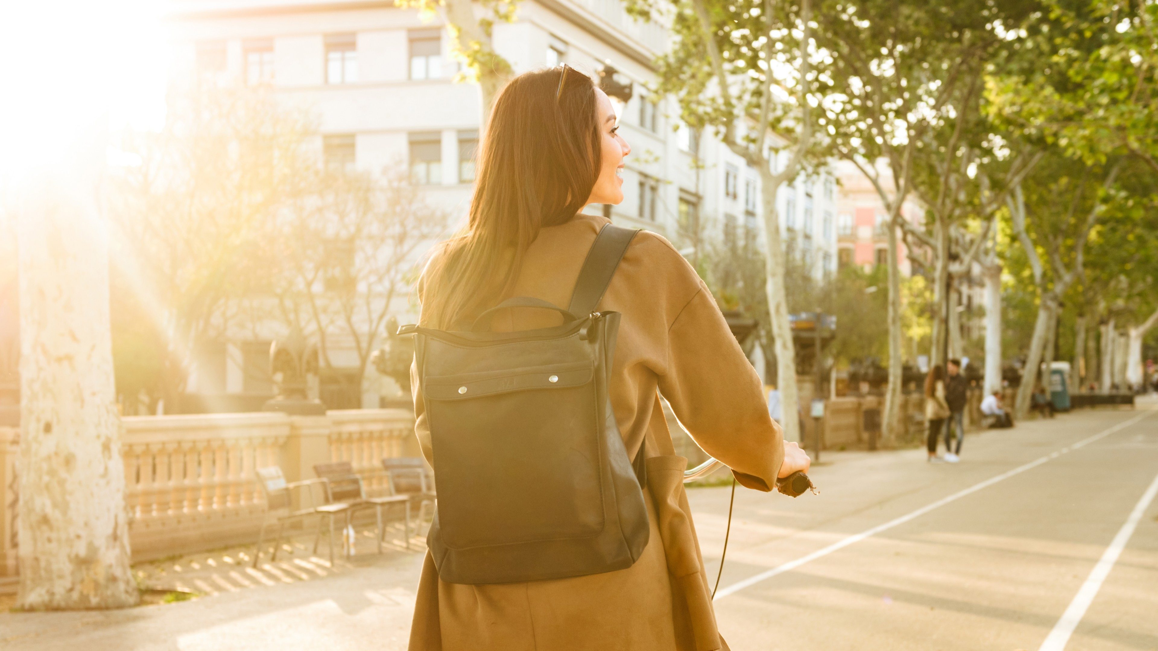 Back view image of young lady outdoors walking on bicycle on the street.