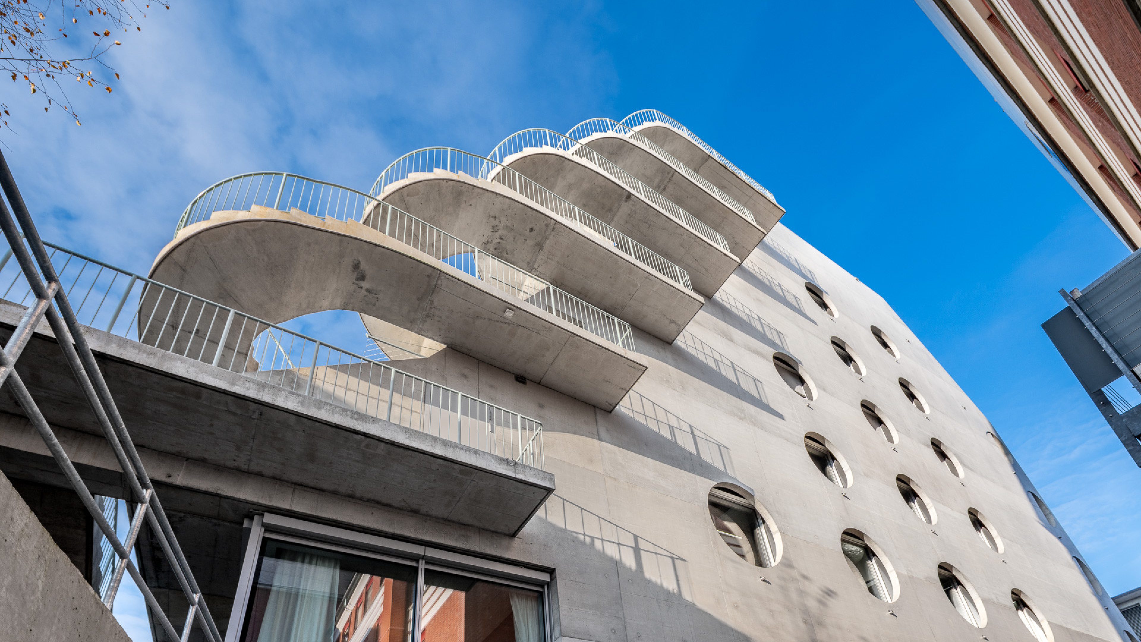 Immeuble moderne en béton avec des balcons incurvés et des fenêtres rondes.