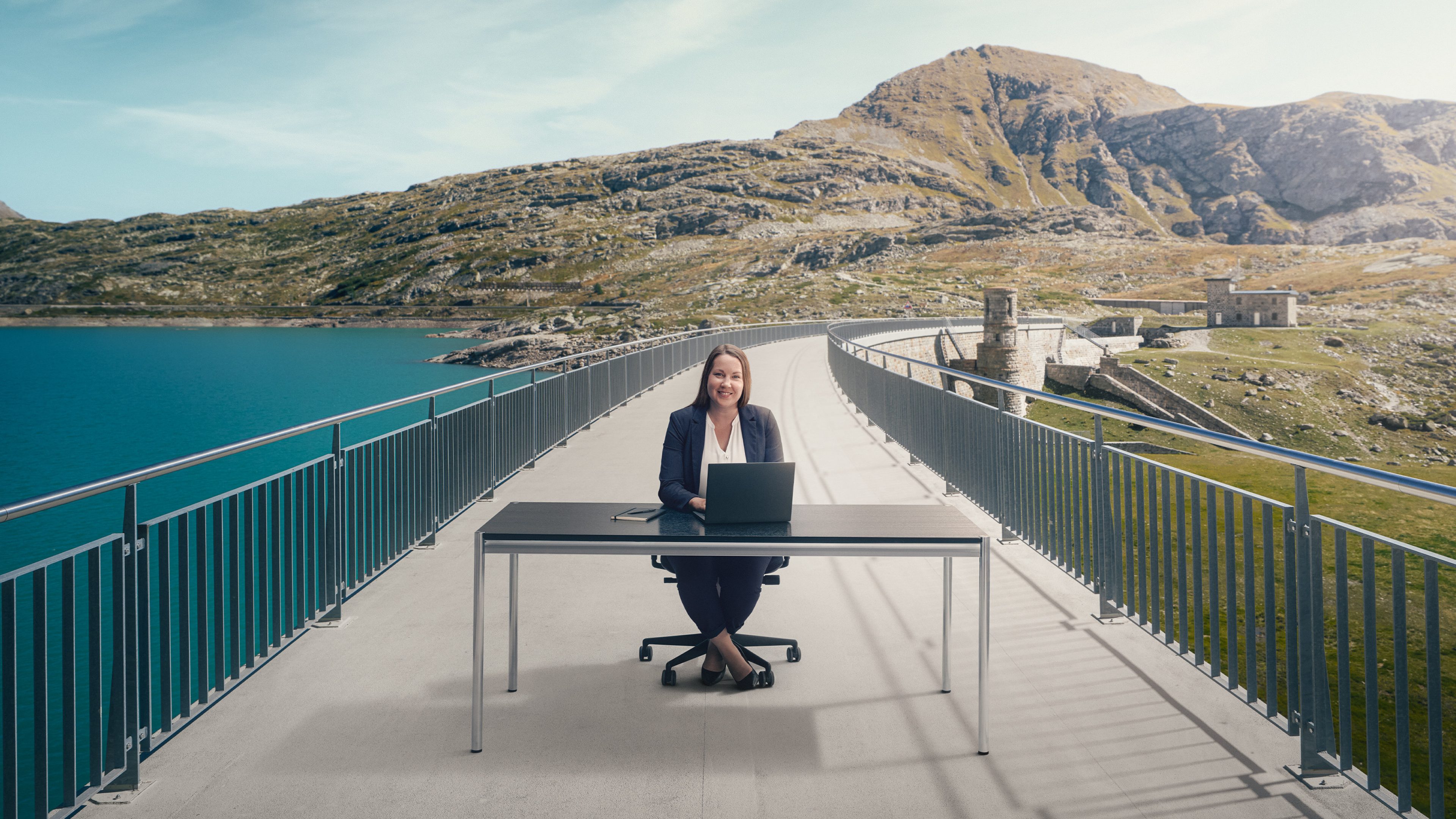 Femme travaillant sur un ordinateur portable à un bureau sur un pont dans un paysage alpin de montagne.