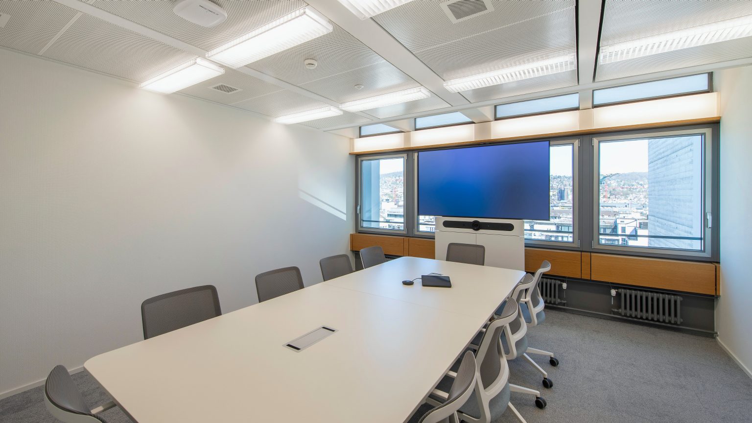 A meeting room with a large table in the middle and a screen with a camera.