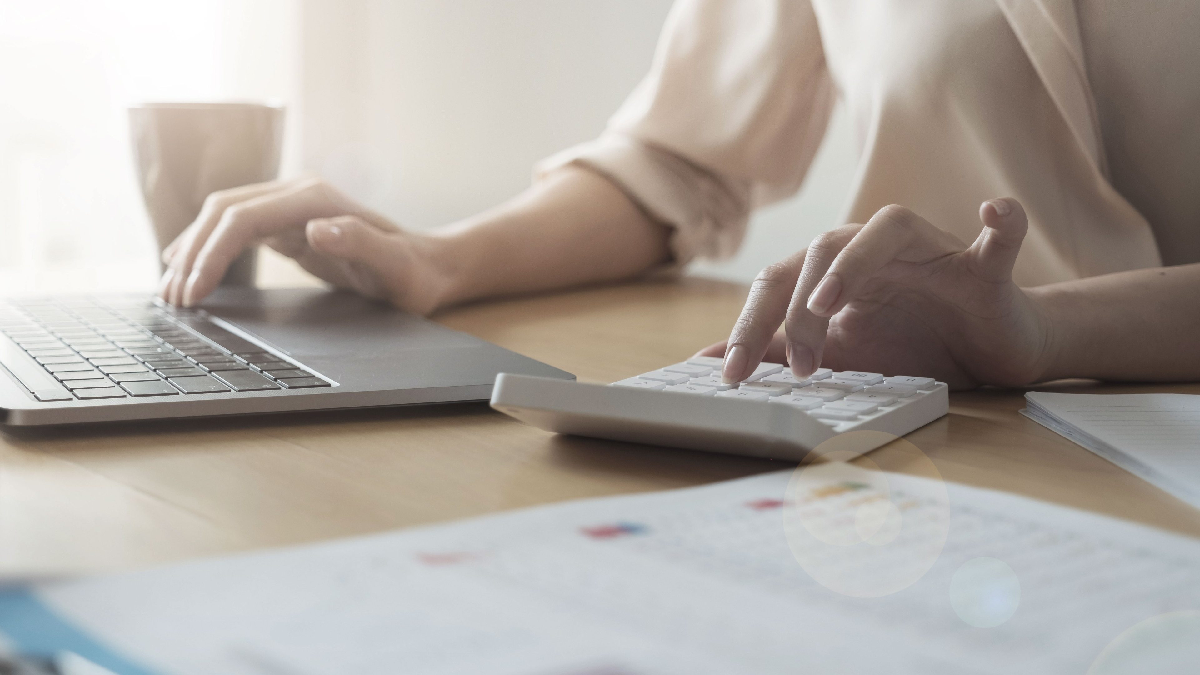 Una persona seduta davanti al proprio computer portatile, con dei documenti davanti a sé.