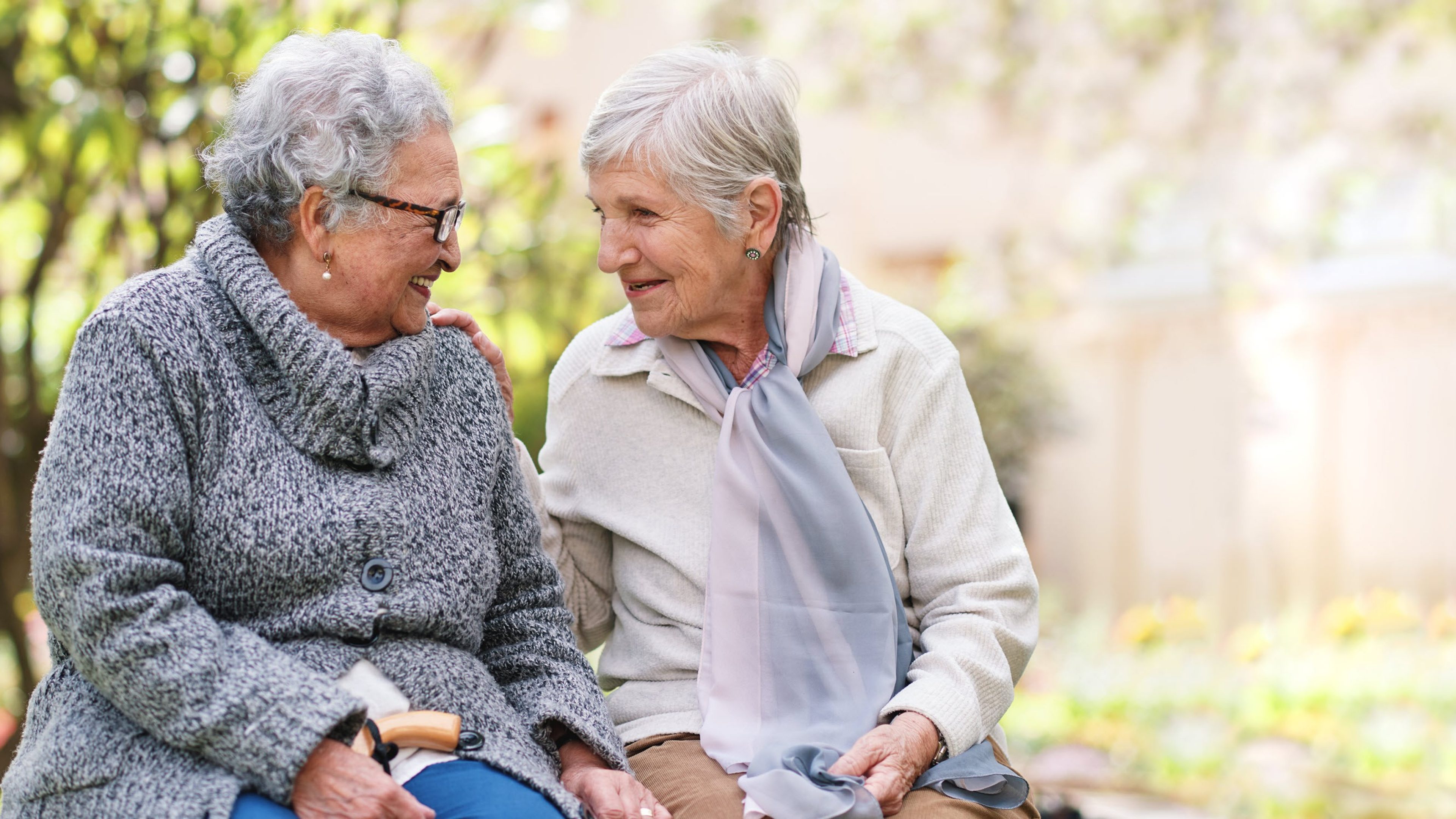 Deux femmes âgées assises sur un banc dans un parc sourient, heureuses d'être des amies de longue date et de profiter de leur retraite.