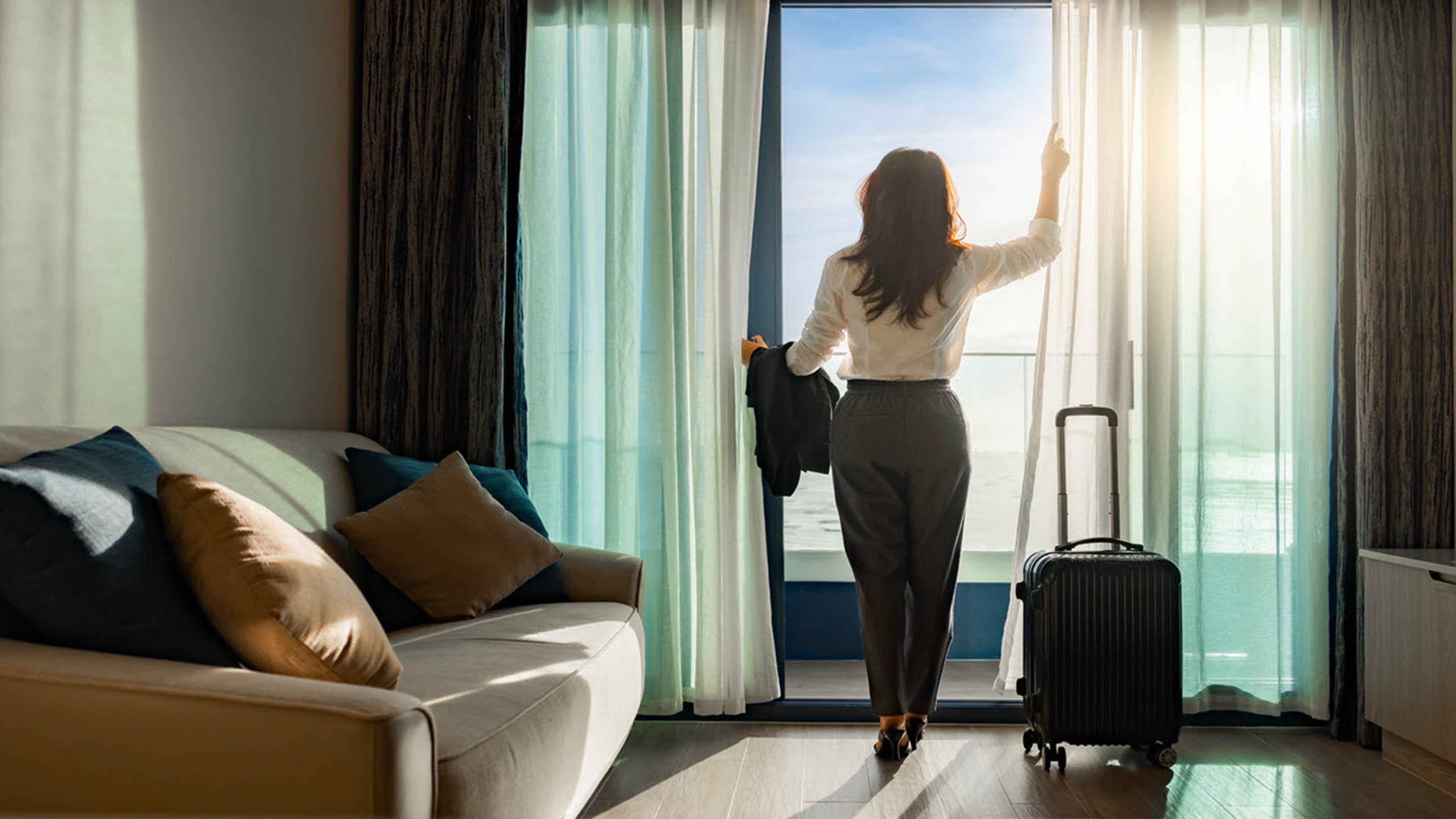 Une femme qui se tient à la fenêtre d'une chambre d'hôtel.